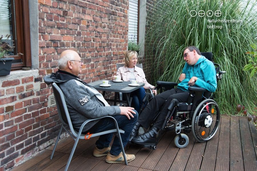 Eltern und ihr Sohn im Rollstuhl sitzen auf einer Terrasse