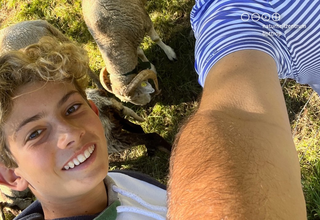 You can see the head of a smiling boy and a sheep in the background