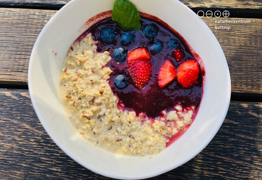 Teller mit Porridge, Nüssen  und frischen Beeren auf einem Holztisch