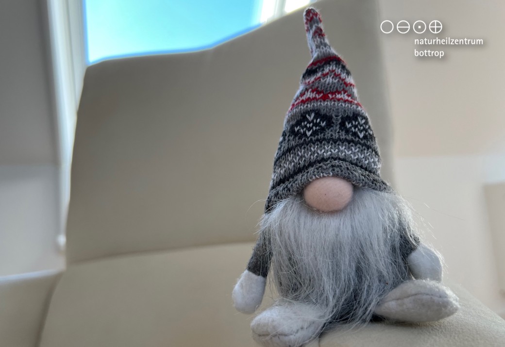 Cute gnome made of wool sits on the armrest of white armchair