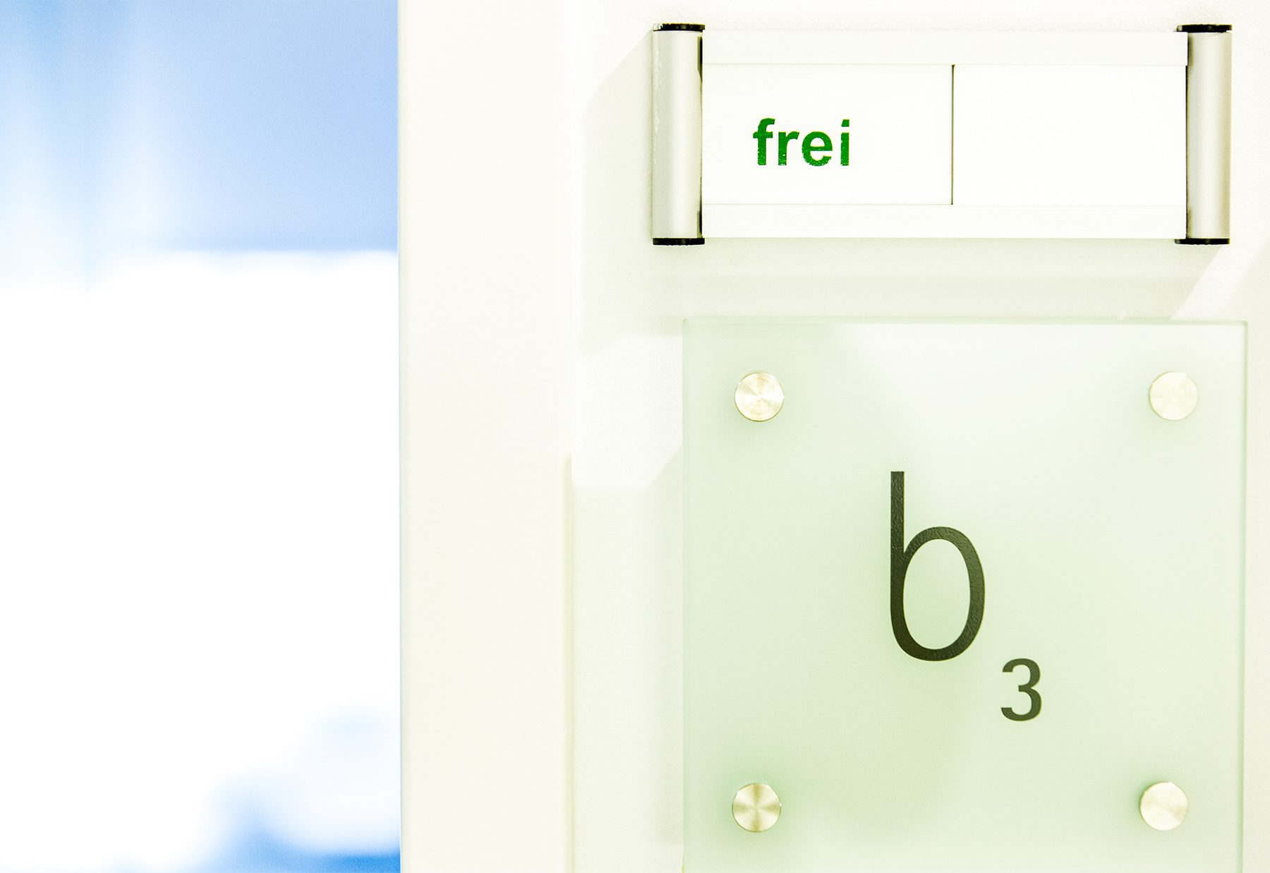 Ein Türschild mit der Aufschrift frei oben und der Kennzeichnung b3 auf einem matte-glänzenden Hintergrund, mit vier silberfarbenen Befestigungen.